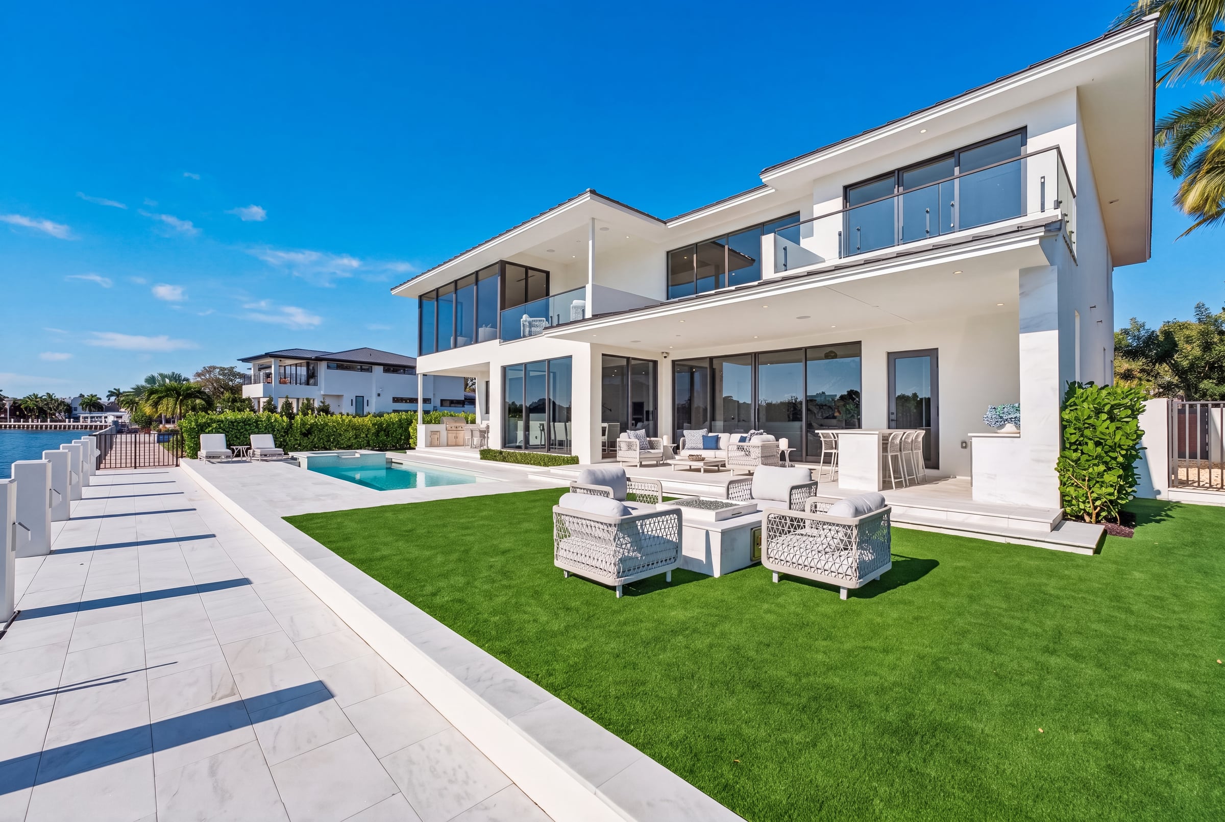 Modern waterfront home opening to a manicured lawn, pool deck, covered lounge, and dock